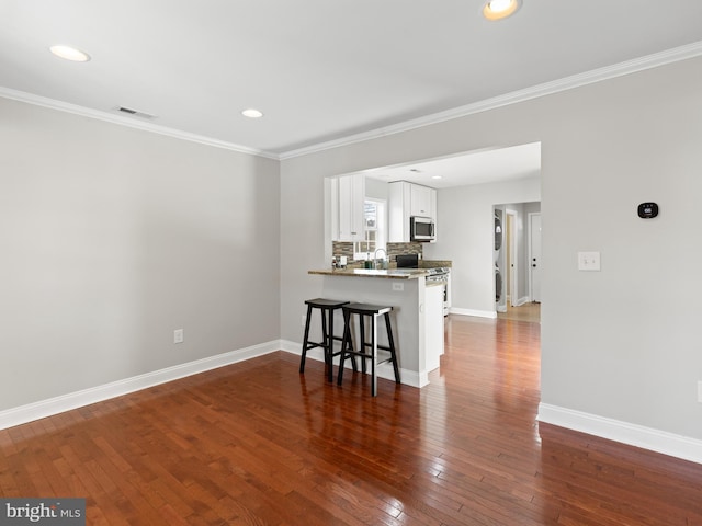 kitchen featuring dark hardwood / wood-style floors, white cabinets, a kitchen breakfast bar, kitchen peninsula, and stainless steel appliances