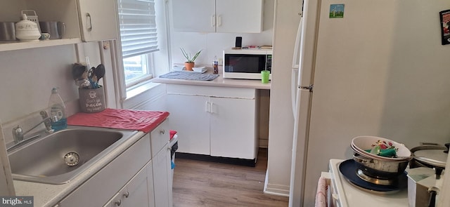 kitchen with sink, white appliances, white cabinets, and light wood-type flooring