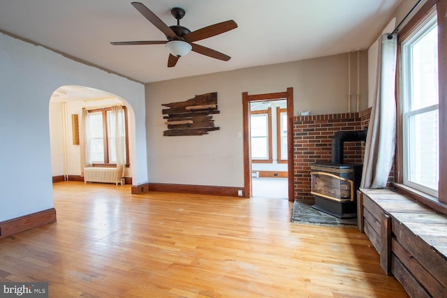 264 S Main St, Pleasant Gap, PA 16823 - unfurnished living room featuring light wood-style flooring, arched walkways, radiator heating unit, ceiling fan, and a wood stove