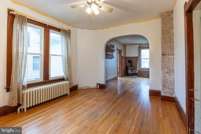 264 S Main St, Pleasant Gap, PA 16823 - unfurnished room featuring light wood-style floors, ceiling fan, arched walkways, a wood stove, and radiator