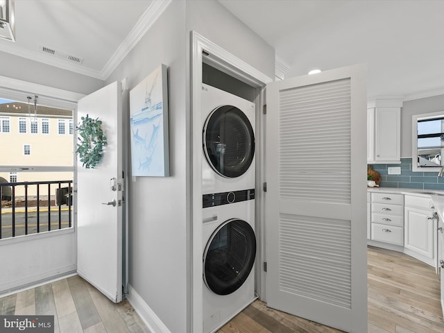 washroom featuring stacked washer and dryer, ornamental molding, and light hardwood / wood-style flooring