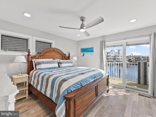 bedroom featuring access to outside, light hardwood / wood-style floors, ceiling fan, and a water view