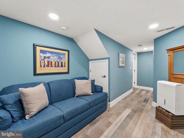 living room featuring vaulted ceiling, heating unit, and light hardwood / wood-style flooring