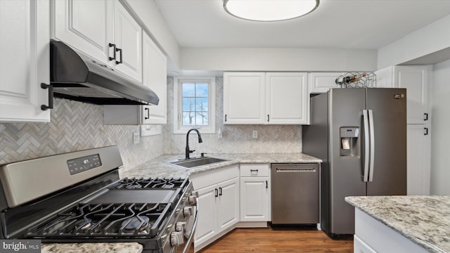 kitchen with appliances with stainless steel finishes, white cabinetry, sink, hardwood / wood-style flooring, and light stone counters