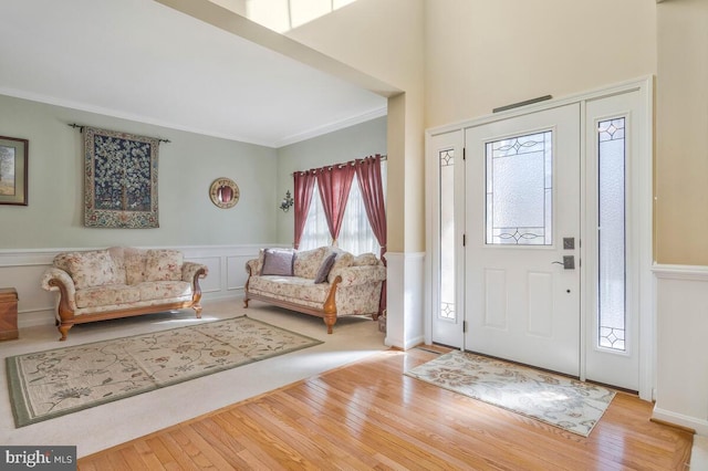 foyer entrance with ornamental molding, a wainscoted wall, and light wood-style floors