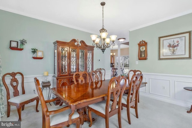 dining room with light colored carpet, a wainscoted wall, crown molding, a chandelier, and a decorative wall