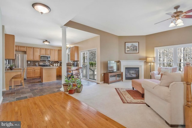 living area featuring ceiling fan, stone finish floor, a glass covered fireplace, and ornate columns