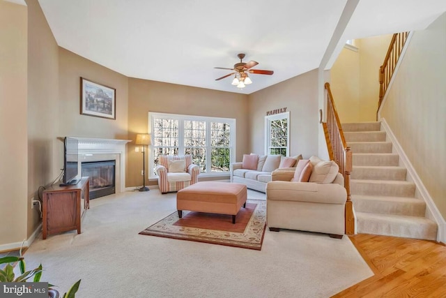 living area featuring stairway, a fireplace with flush hearth, a ceiling fan, and baseboards