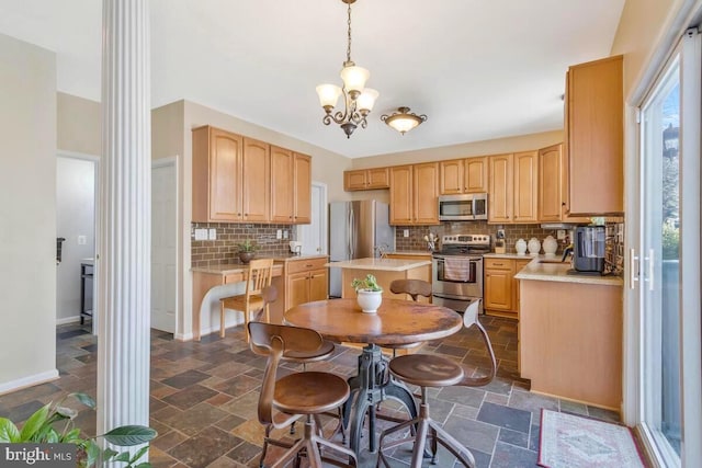 kitchen with hanging light fixtures, stone tile floors, stainless steel appliances, and light countertops