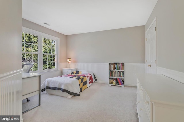 bedroom with wainscoting, visible vents, and light carpet