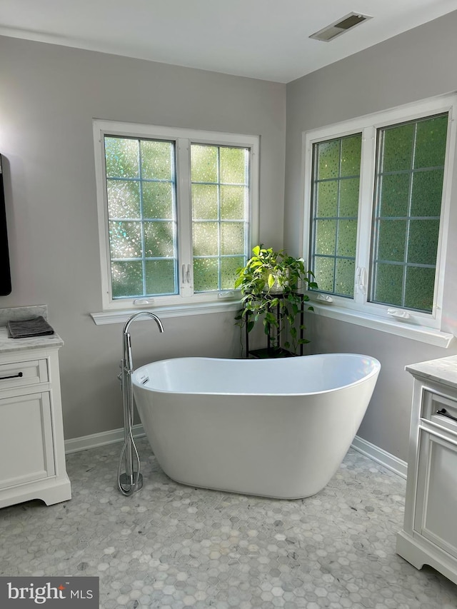 bathroom featuring a soaking tub, vanity, visible vents, and baseboards