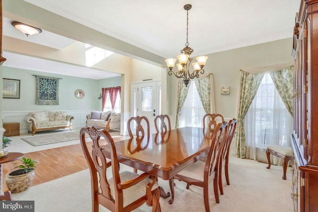 dining area featuring light wood finished floors, light colored carpet, wainscoting, a chandelier, and a decorative wall