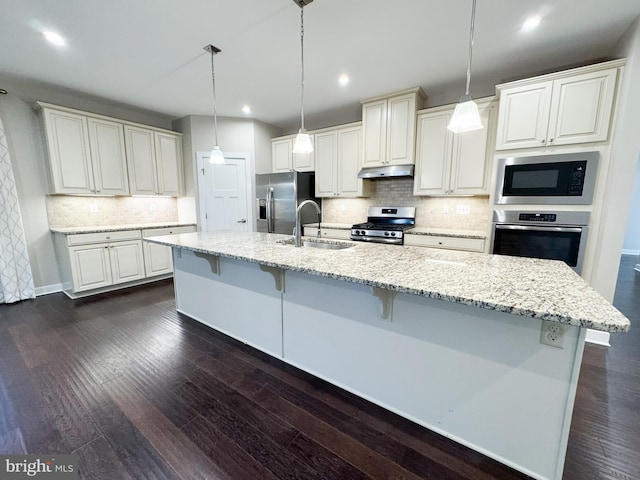 kitchen with stainless steel appliances, light stone countertops, hanging light fixtures, and a kitchen island with sink