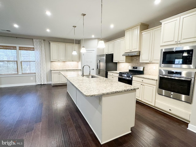 kitchen featuring pendant lighting, an island with sink, sink, stainless steel appliances, and dark wood-type flooring