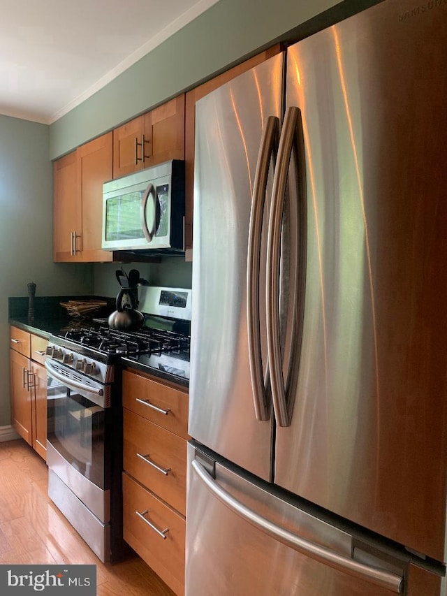 kitchen with dark stone countertops, crown molding, light hardwood / wood-style flooring, and stainless steel appliances