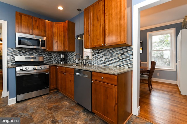 kitchen with sink, light stone counters, pendant lighting, stainless steel appliances, and backsplash