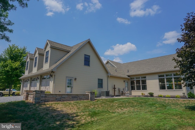 back of property with a garage, central AC, and a lawn