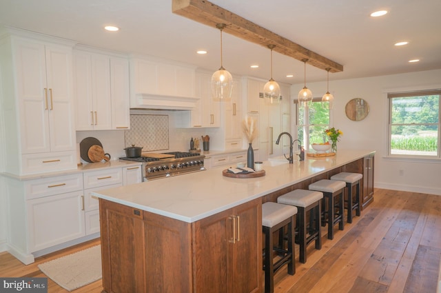 kitchen featuring white cabinetry, range, hanging light fixtures, a large island with sink, and backsplash