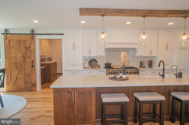 kitchen with hanging light fixtures, light wood-type flooring, a barn door, a kitchen island with sink, and white cabinets