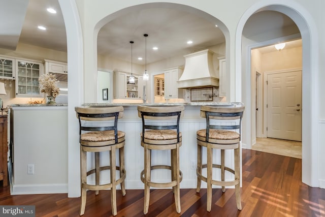 kitchen featuring premium range hood, a kitchen bar, decorative light fixtures, dark hardwood / wood-style floors, and white cabinets