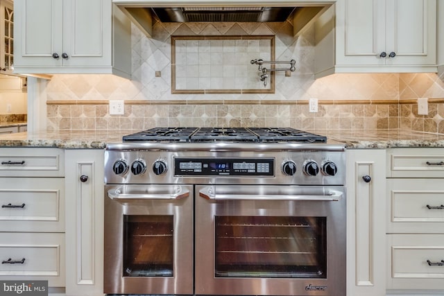 kitchen with double oven range, light stone countertops, exhaust hood, and white cabinets