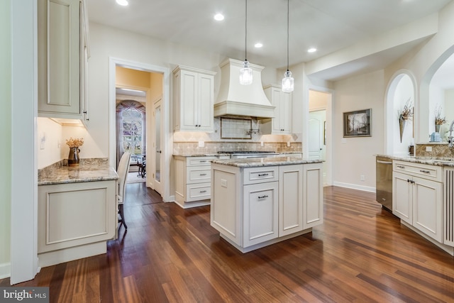 kitchen with a kitchen island, white cabinetry, custom exhaust hood, hanging light fixtures, and light stone counters