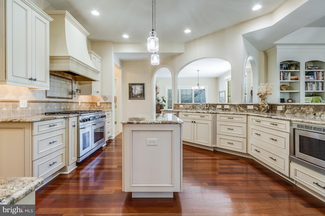 kitchen featuring custom range hood, appliances with stainless steel finishes, a center island, and light stone countertops