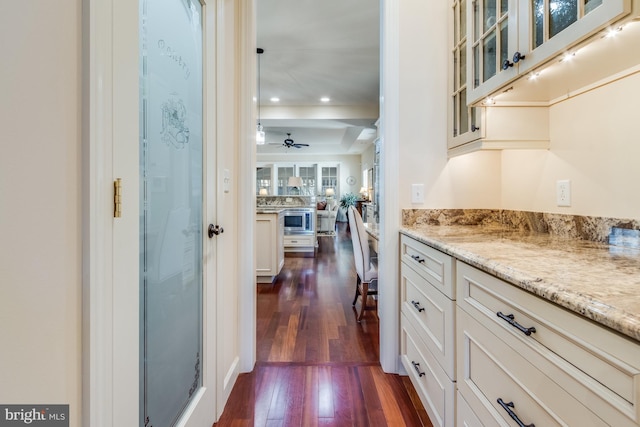 kitchen featuring stainless steel microwave, white cabinetry, dark hardwood / wood-style flooring, ceiling fan, and light stone counters