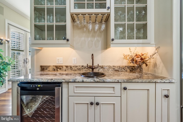 bar with sink, hardwood / wood-style floors, light stone counters, white cabinets, and beverage cooler