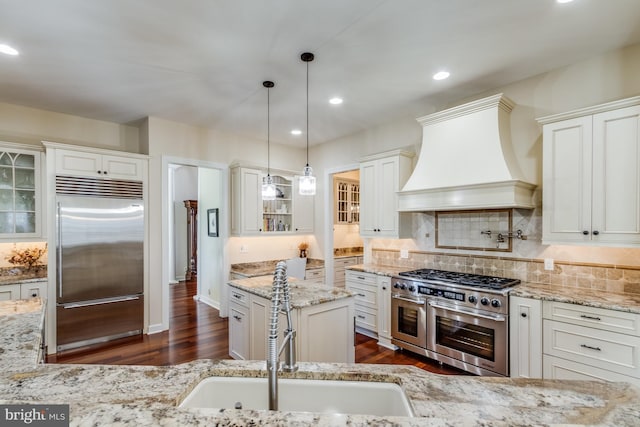 kitchen featuring custom exhaust hood, light stone counters, premium appliances, pendant lighting, and white cabinets