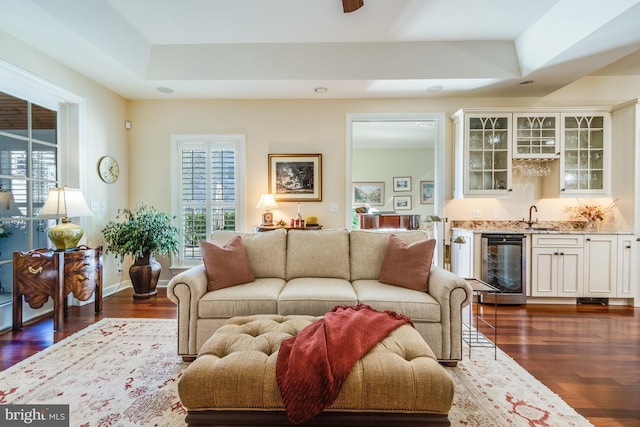 living room featuring dark hardwood / wood-style floors, indoor wet bar, wine cooler, and a tray ceiling