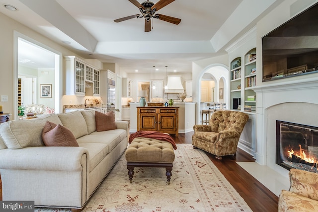 living room featuring hardwood / wood-style flooring, a raised ceiling, sink, and built in features