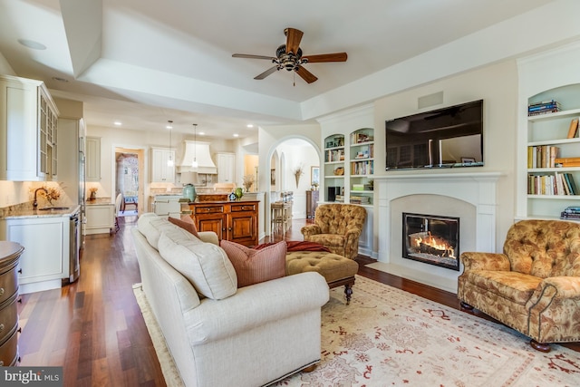 living room featuring a raised ceiling, sink, dark hardwood / wood-style flooring, and built in shelves