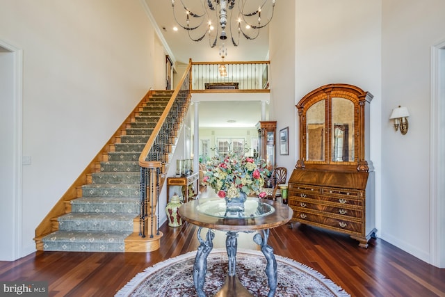 foyer with a high ceiling, crown molding, dark hardwood / wood-style floors, and an inviting chandelier