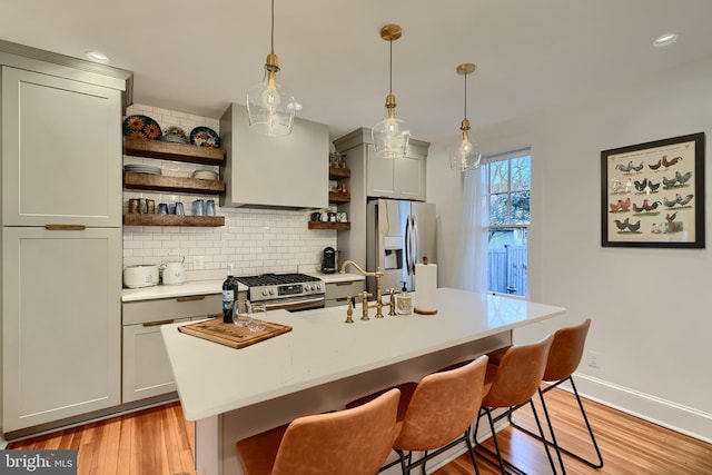 kitchen with pendant lighting, appliances with stainless steel finishes, a kitchen breakfast bar, and exhaust hood