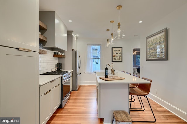 kitchen featuring pendant lighting, an island with sink, a kitchen breakfast bar, stainless steel appliances, and wall chimney exhaust hood