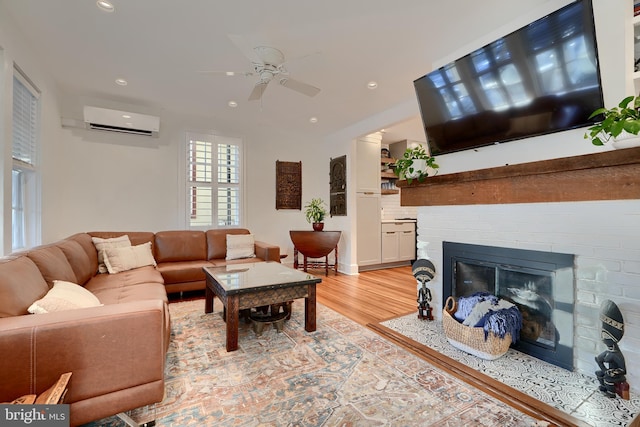 living room featuring light hardwood / wood-style flooring, ceiling fan, a fireplace, and a wall mounted AC