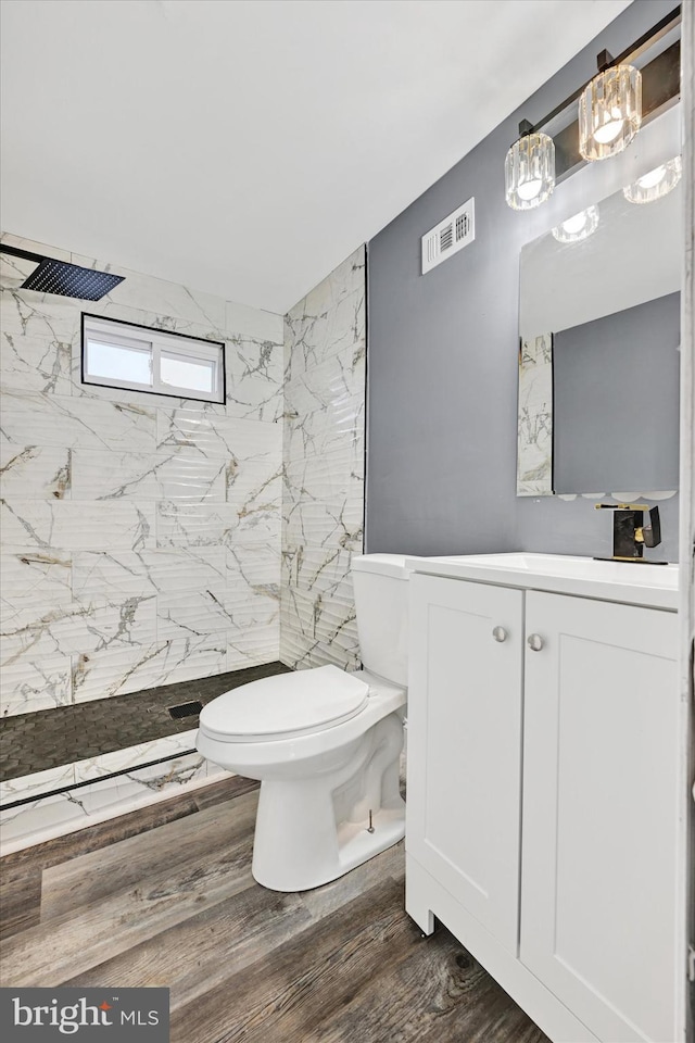 bathroom featuring hardwood / wood-style flooring, vanity, tiled shower, and toilet