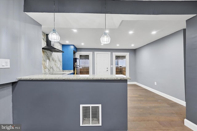 kitchen featuring light stone countertops, kitchen peninsula, hanging light fixtures, and wall chimney range hood