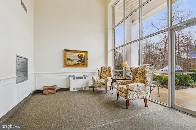 sitting room featuring a towering ceiling, radiator, carpet, and a mail area