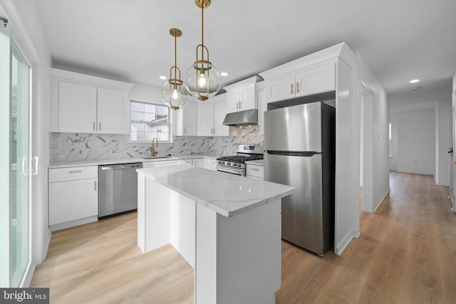 kitchen with appliances with stainless steel finishes, backsplash, a center island, white cabinets, and decorative light fixtures