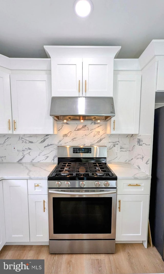 kitchen with light stone counters, white cabinets, range hood, and stainless steel gas range oven