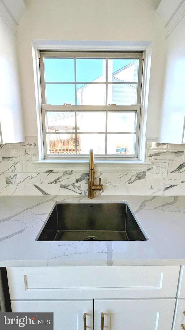 interior details featuring white cabinetry, sink, light stone counters, and decorative backsplash