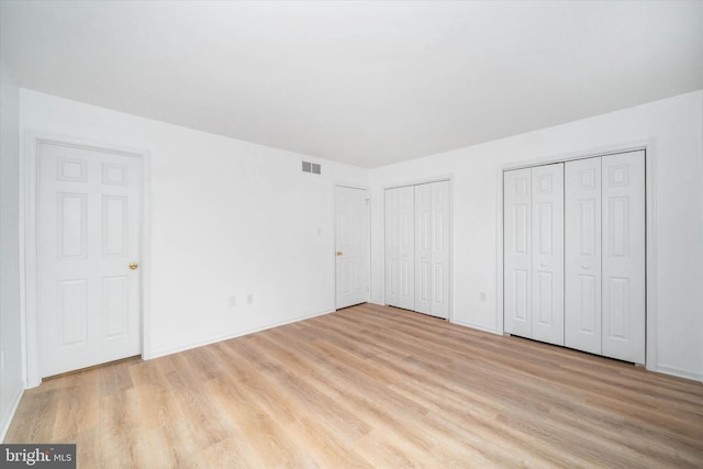 unfurnished bedroom with light hardwood / wood-style floors and multiple closets