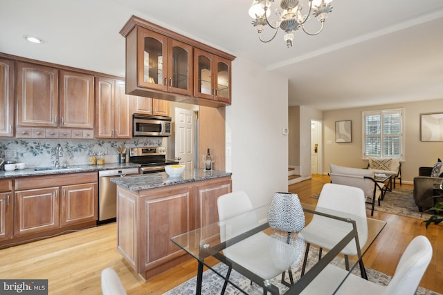 kitchen with sink, appliances with stainless steel finishes, dark stone countertops, a notable chandelier, and decorative backsplash