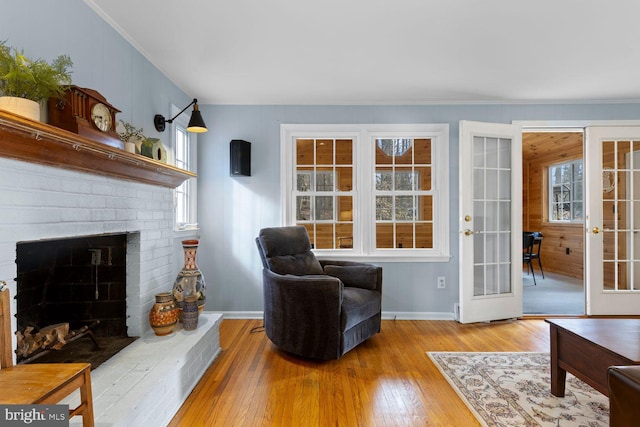 living area with french doors, a fireplace, crown molding, light wood-style flooring, and baseboards