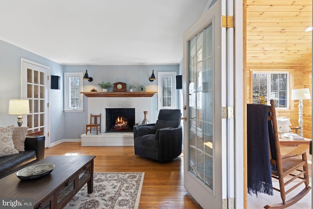 living area with french doors, a brick fireplace, wood finished floors, and baseboards