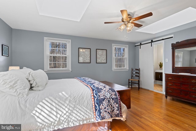 bedroom featuring light wood-style floors, ceiling fan, and a barn door