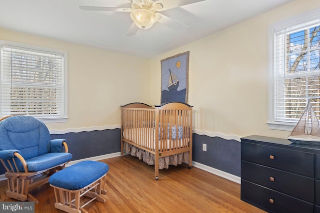 bedroom featuring a crib, light wood finished floors, ceiling fan, and baseboards