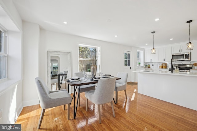 dining room featuring arched walkways, recessed lighting, baseboards, and light wood-style floors